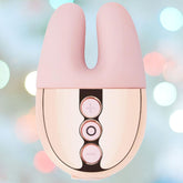 Image of a Rose Gold Le Wand Chrome Double Motor Vibrator with three vertically arranged buttons on its front side. The background is blurred with soft bokeh lights in pastel colors.